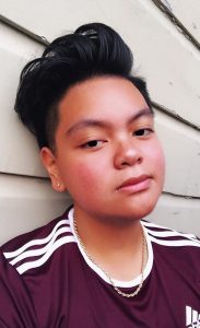 Image description: JoJo is leaning against a wall, head tilted slightly and looking at the camera.